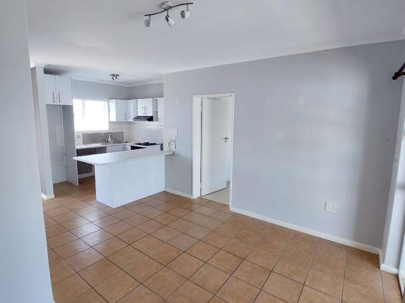 An open-plan living and kitchen area featuring neutral wall tones, tiled flooring, and a functional kitchen layout with built-in cabinetry and a breakfast bar.