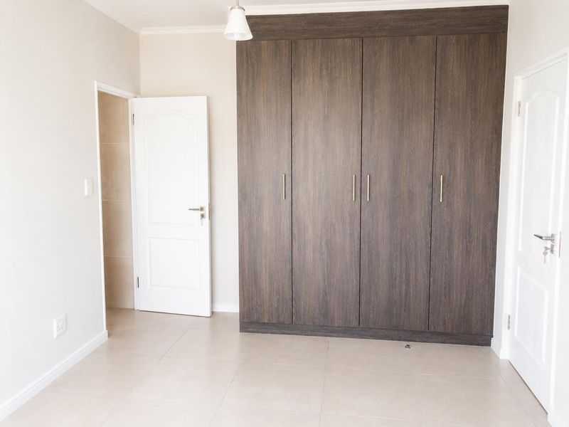 A clean, empty bedroom featuring modern dark wood built-in cupboards, neutral tiled flooring, and crisp white walls.