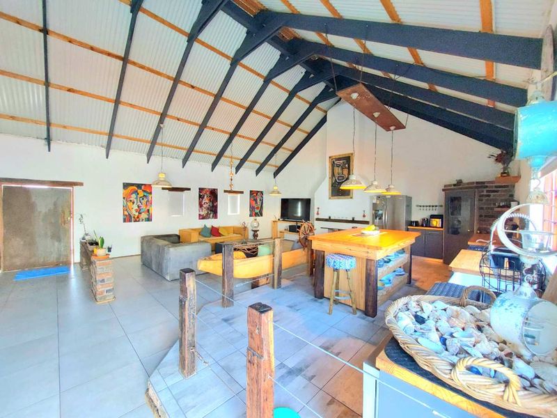 Spacious open-plan living area featuring high vaulted ceilings with exposed rafters, tiled floors, a central kitchen island, and a brick fireplace.
