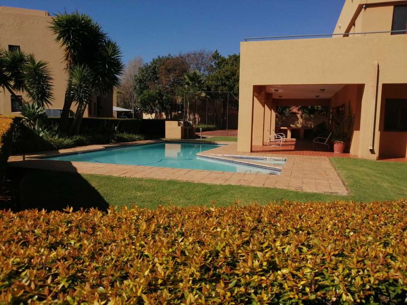 Outdoor pool area featuring a swimming pool, paved surround, and a covered patio with a built-in braai, set within a landscaped garden.