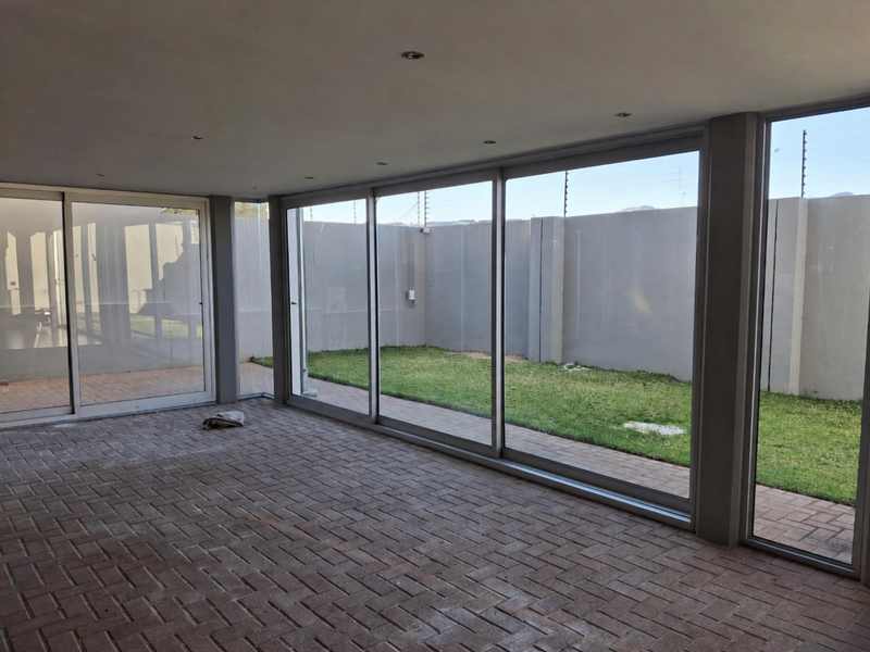 A spacious, enclosed patio featuring large sliding glass doors, brick paving, and recessed lighting, offering a seamless transition to the private rear garden.