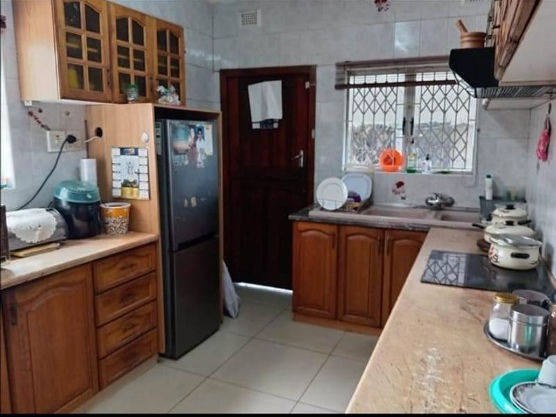 A functional kitchen featuring wooden cabinetry, laminate countertops, a double sink, and an integrated electric hob with an extractor fan.