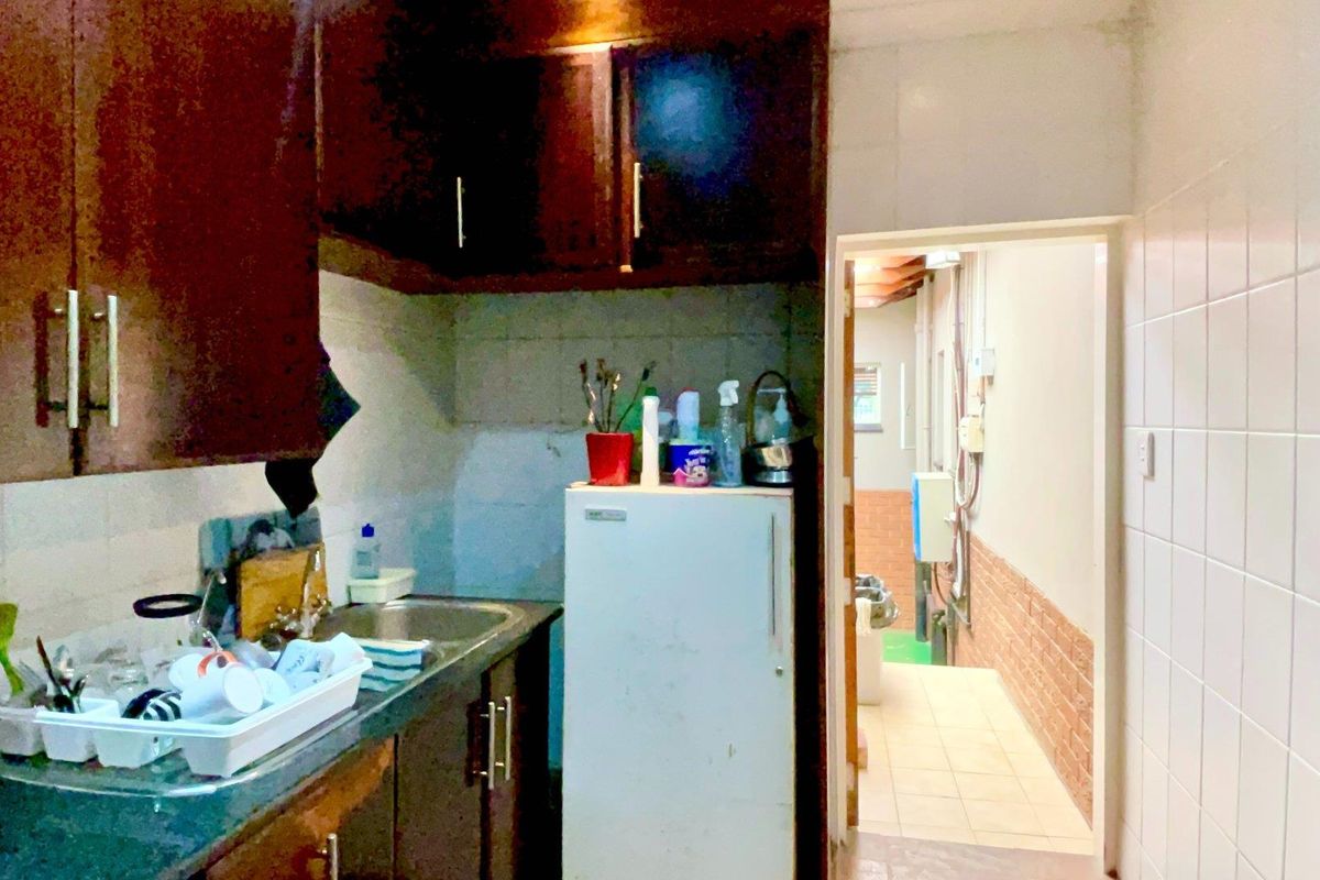 A compact kitchen featuring dark wood cabinetry, tiled splashbacks, and a stainless steel sink, with an adjacent utility area visible through the doorway.