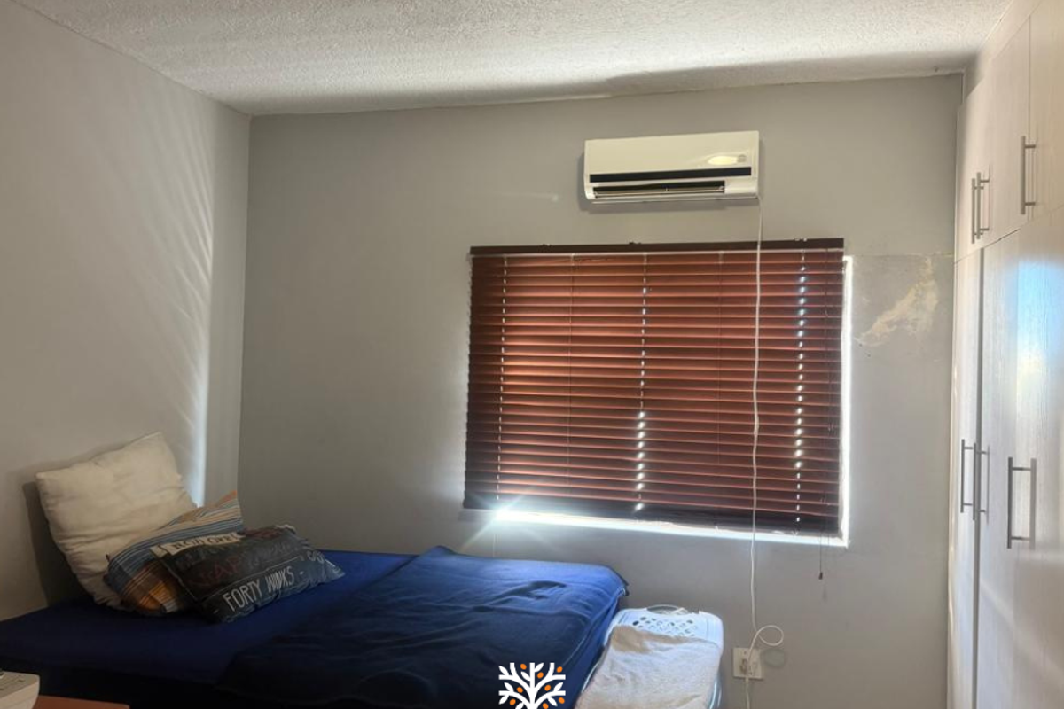 A bedroom featuring built-in wardrobes, a wall-mounted air conditioning unit, and window blinds.