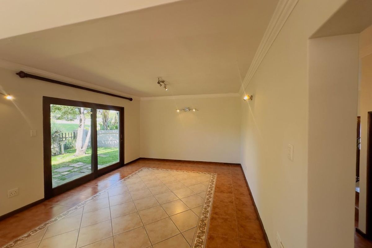 A bright, empty living area featuring tiled flooring with decorative border inlay and large sliding glass doors providing direct access to the garden.