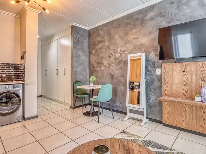 Open plan living area featuring tiled floors, a textured feature wall, built-in cabinetry, and a dedicated laundry nook with integrated washing machine.