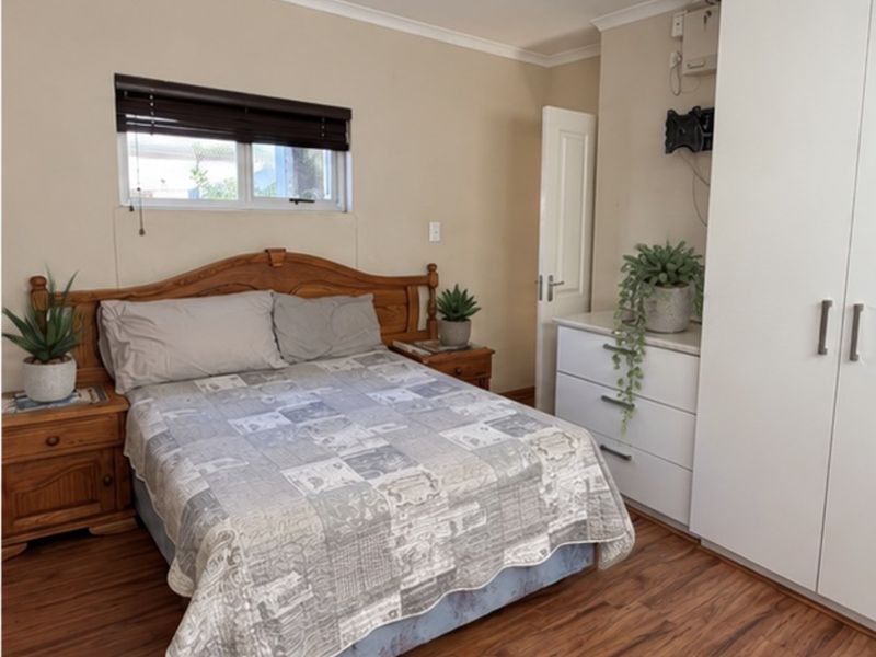 A functional bedroom featuring laminate flooring, a built-in wardrobe, and a window with a venetian blind.