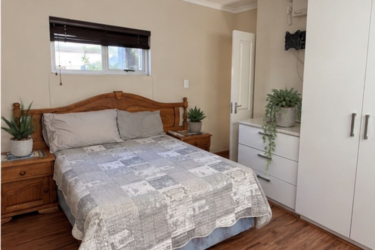 A functional bedroom featuring laminate flooring, a built-in wardrobe, and a window with a venetian blind.