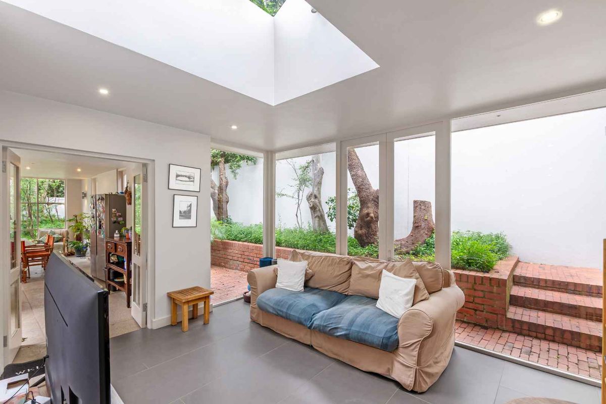 Bright living room featuring a large skylight, floor-to-ceiling windows, and direct access to a private brick-paved courtyard garden.