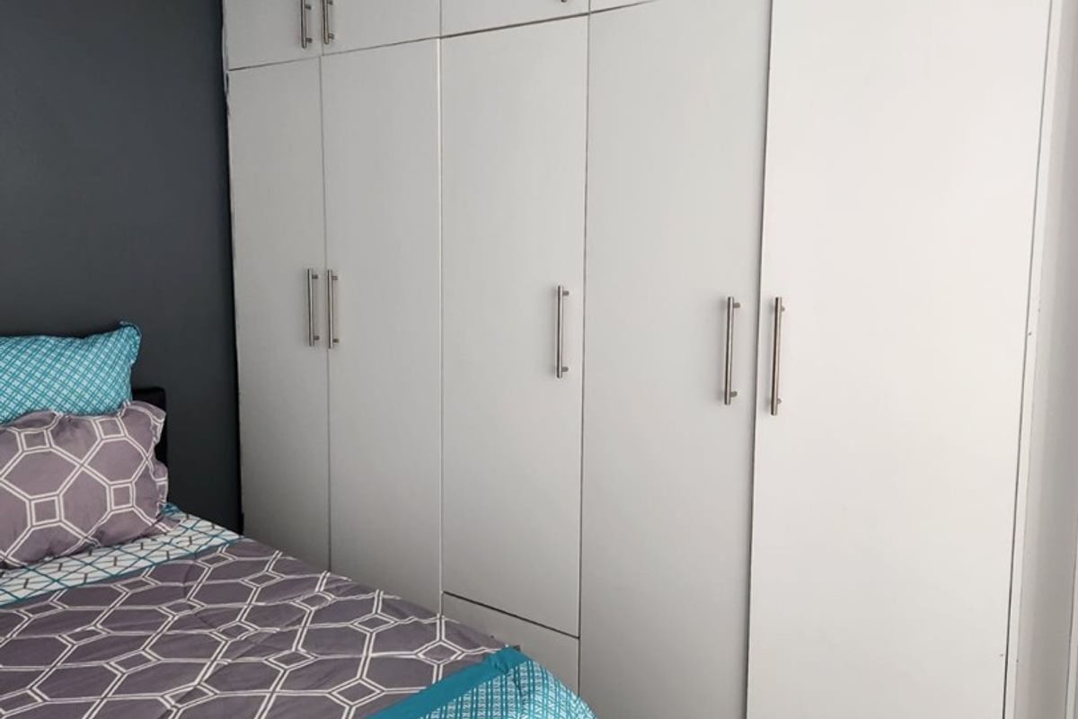 A well-maintained bedroom featuring extensive floor-to-ceiling built-in cupboards and modern laminate flooring.