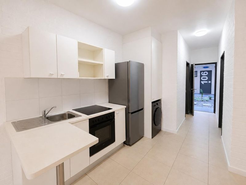 A clean, modern kitchen featuring white cabinetry, built-in oven and cooktop, tiled backsplash, and integrated laundry space, leading directly to the apartment entrance.