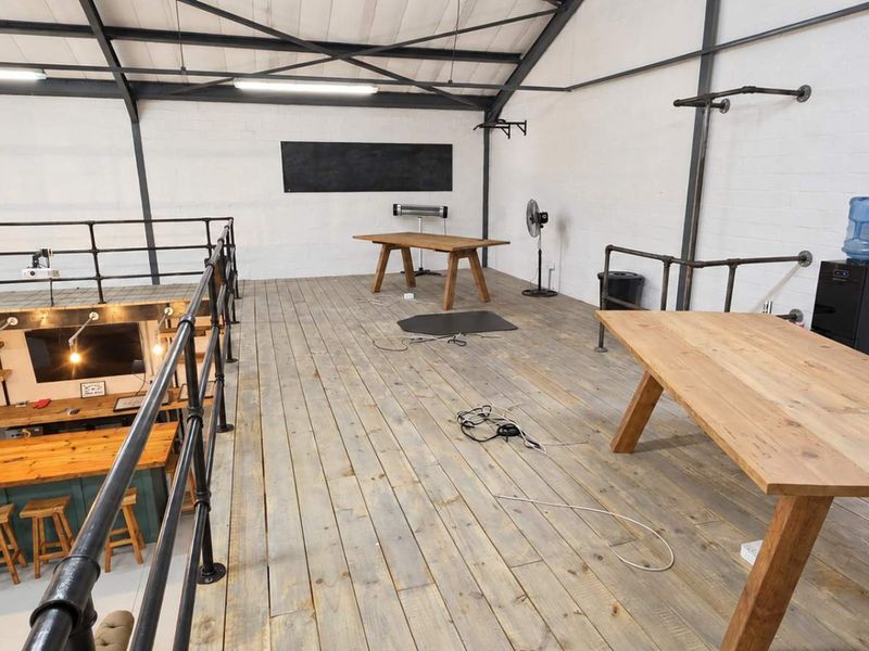 Spacious industrial-style open plan mezzanine level featuring exposed steel trusses, timber flooring, and a lower-level kitchen area with industrial pipe railings.