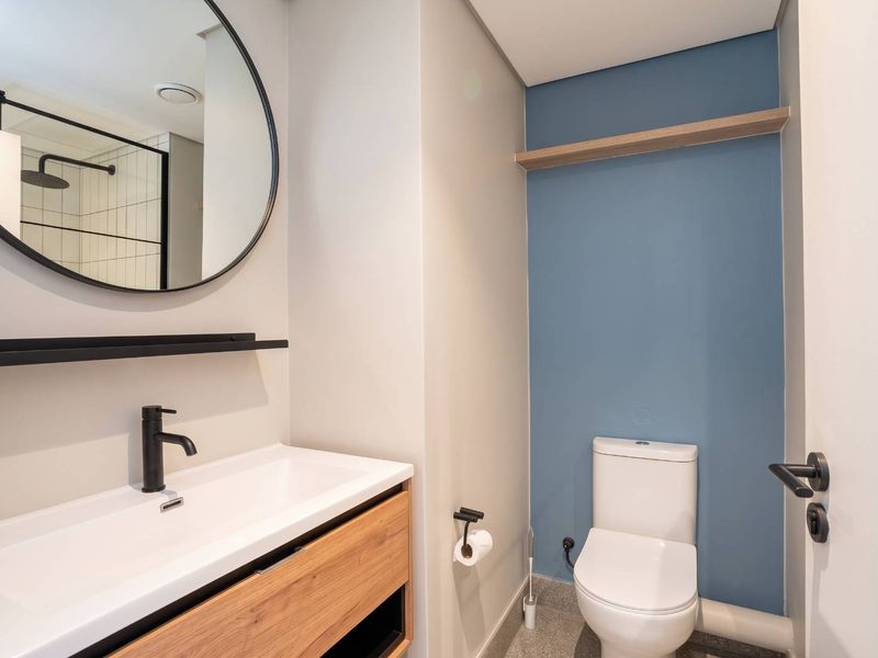 Modern bathroom featuring a vanity with basin, round mirror, toilet, and contemporary matte black fixtures against a blue accent wall.