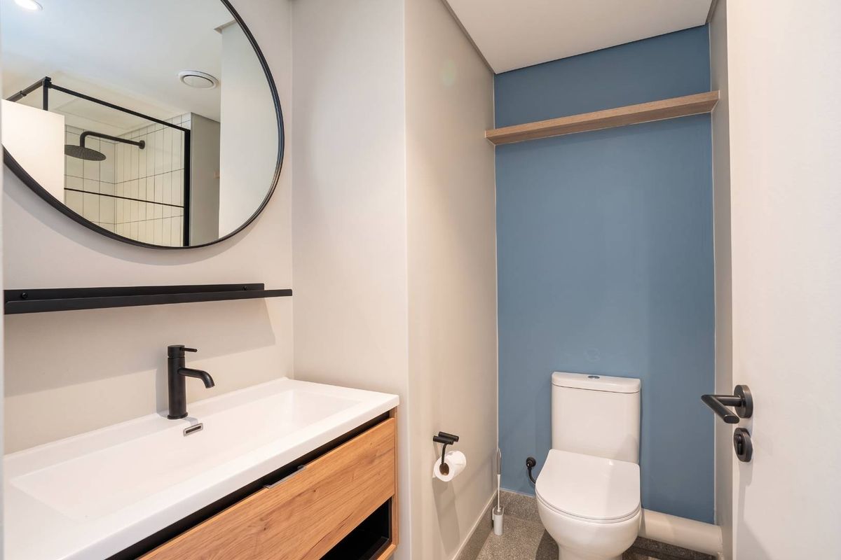 Modern bathroom featuring a vanity with basin, round mirror, toilet, and contemporary matte black fixtures against a blue accent wall.