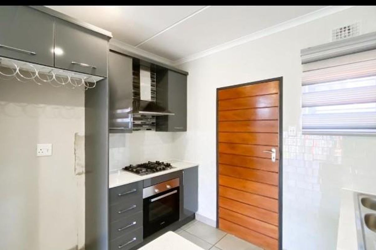 Modern kitchen featuring dark grey cabinetry, built-in gas hob, oven, extractor fan, and tiled flooring with a wooden door entrance.