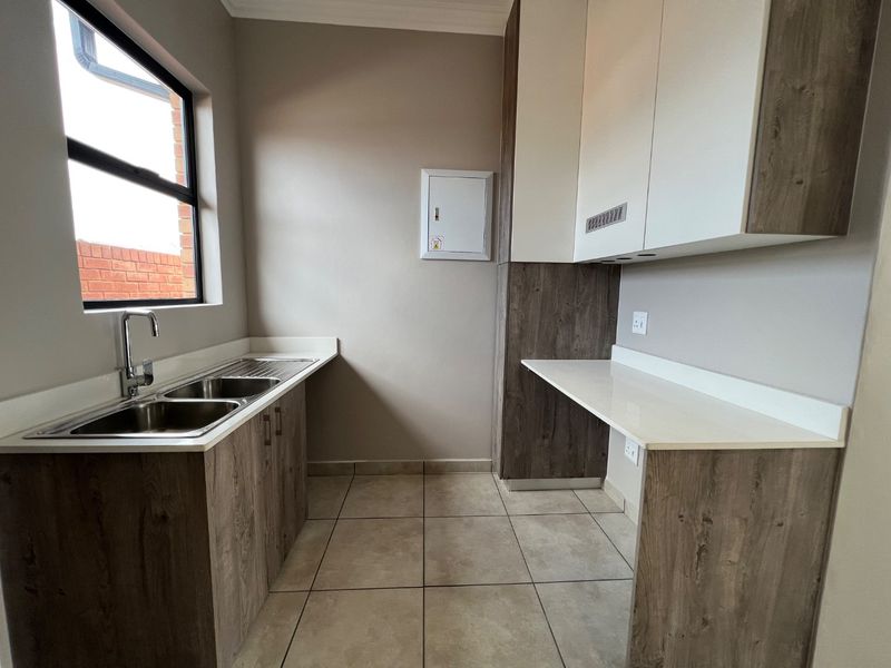 A clean and functional scullery featuring modern laminate cabinetry, stone countertops, a double stainless steel sink, and tiled flooring.