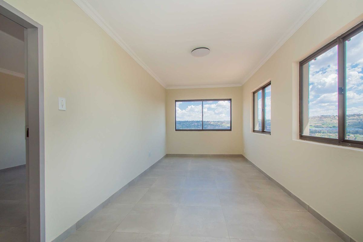 A bright, empty bedroom featuring neutral walls, large windows with scenic views, and modern tiled flooring.