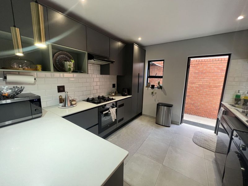 Modern kitchen featuring sleek dark cabinetry, quartz countertops, subway tile backsplash, and integrated appliances, with direct access to an outdoor area.