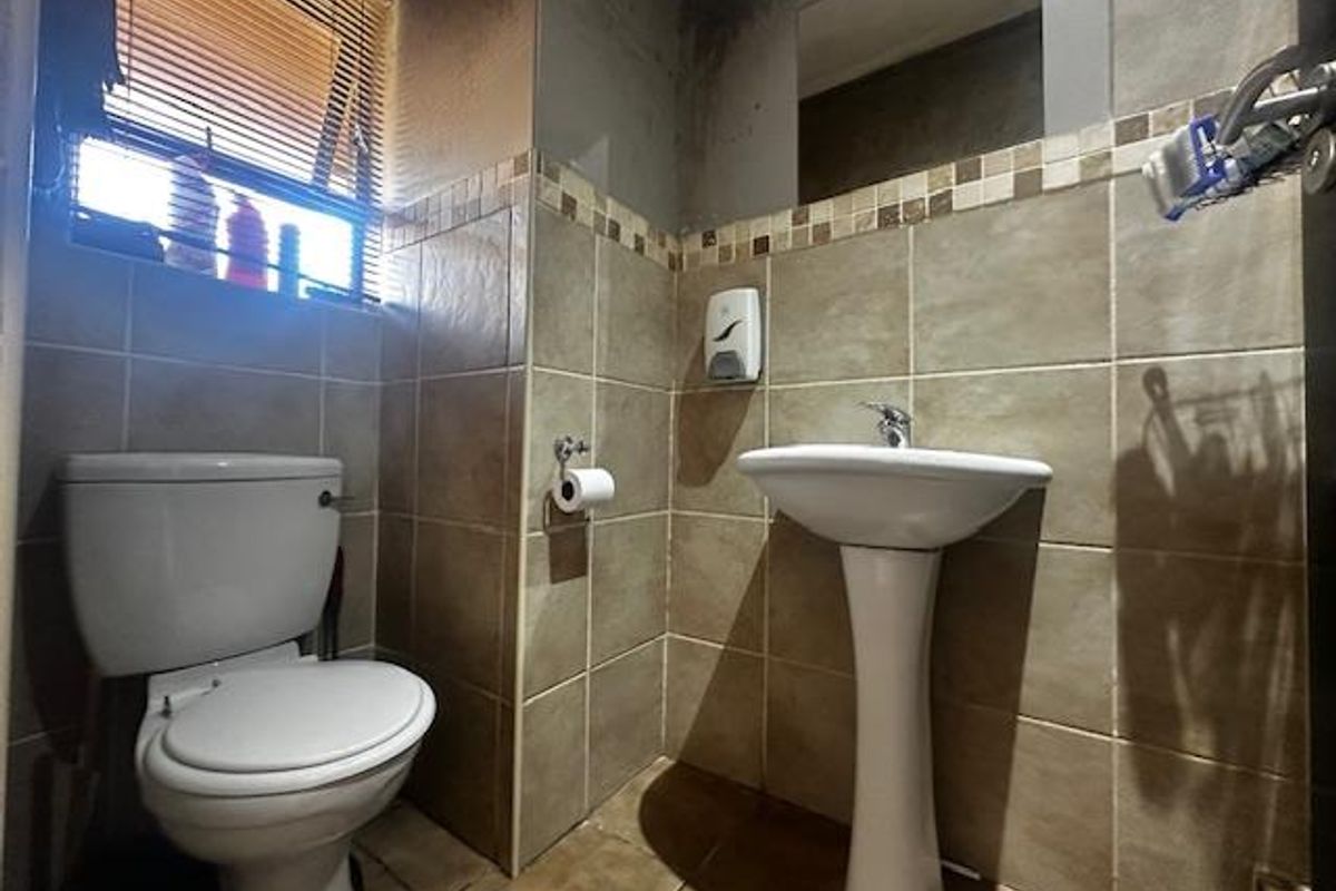 A compact bathroom featuring a pedestal basin, toilet, and tiled finishes. The space requires maintenance due to visible wall staining.