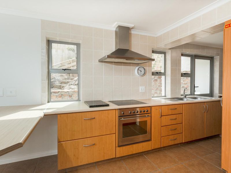 A functional kitchen featuring wooden cabinetry, stainless steel appliances, tiled splashbacks, and tiled flooring with direct access to the exterior.