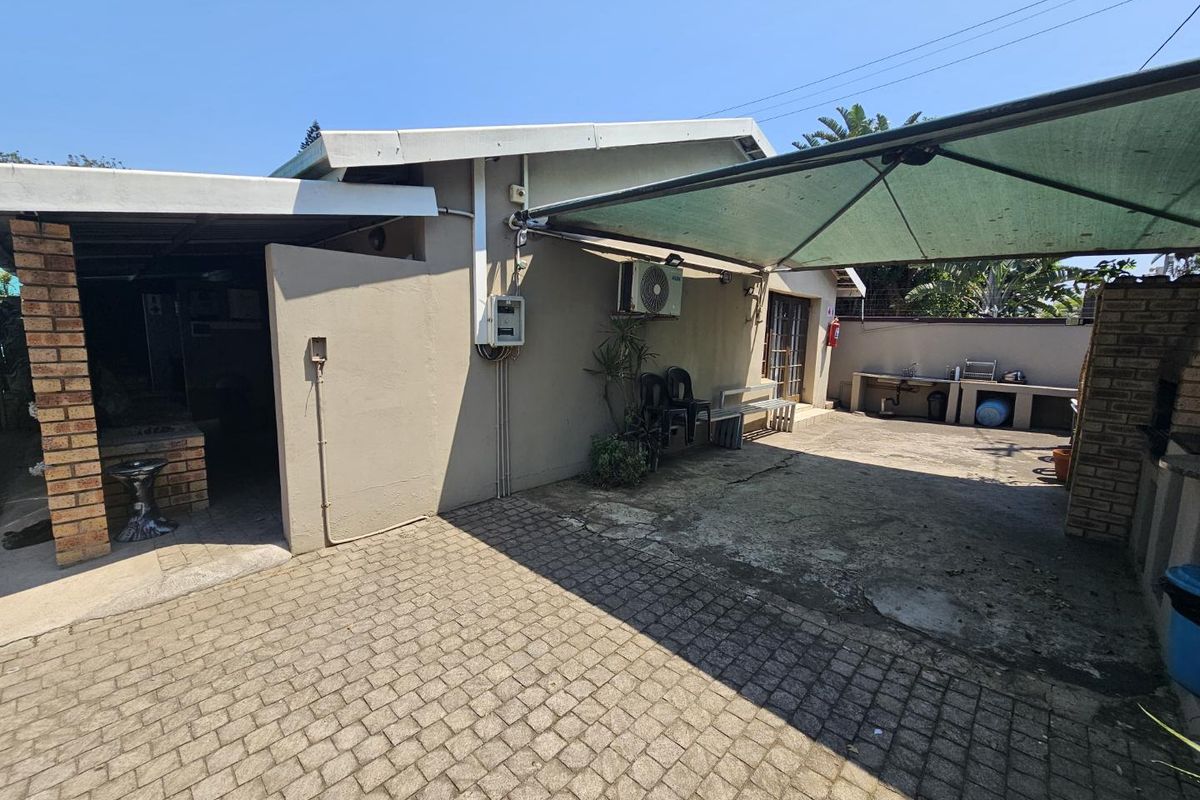 Rear exterior area featuring paved flooring, a built-in braai, outdoor sink, and a shade sail structure.