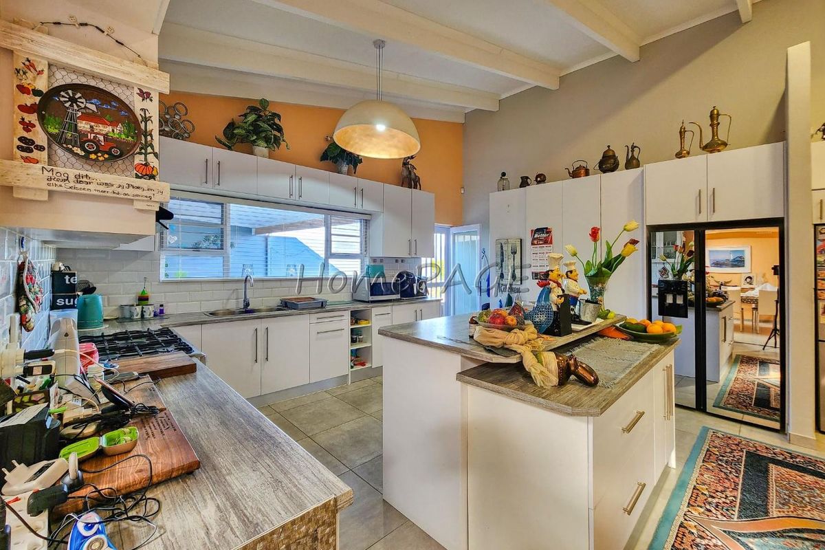 Spacious kitchen featuring a central island, white cabinetry, gas hob, extractor fan, and tiled flooring under exposed ceiling beams.