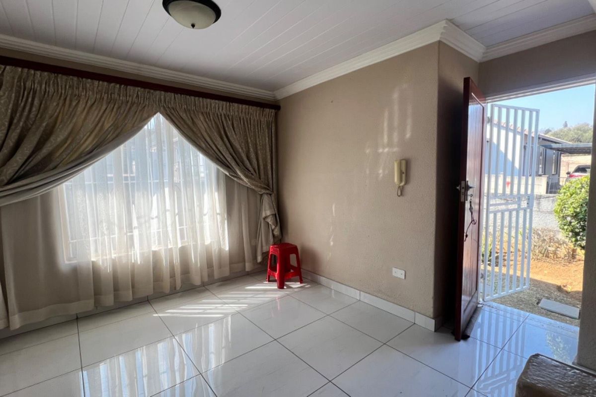 A bright, empty living area featuring tiled flooring, ceiling cornices, and direct access to the exterior through a secure entrance door.