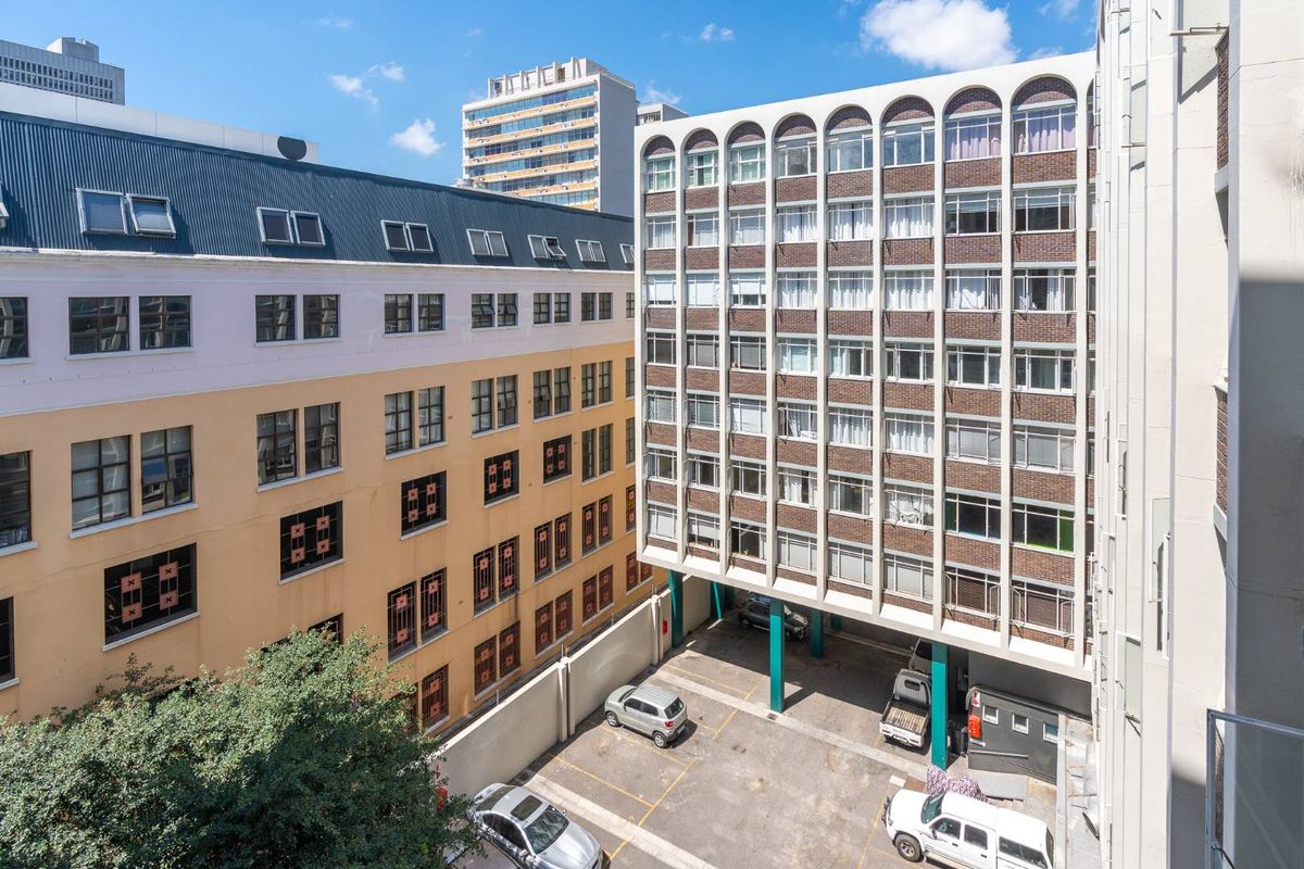 An elevated view of the apartment building exterior, featuring a ground-level parking area and surrounding urban architecture.