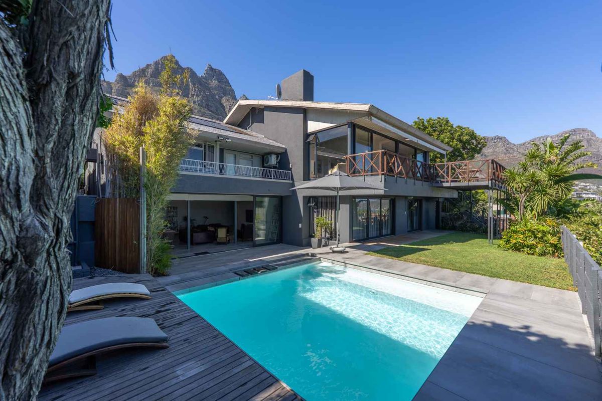 Rear exterior view featuring a swimming pool, timber decking, landscaped garden, and a multi-level balcony with mountain views.