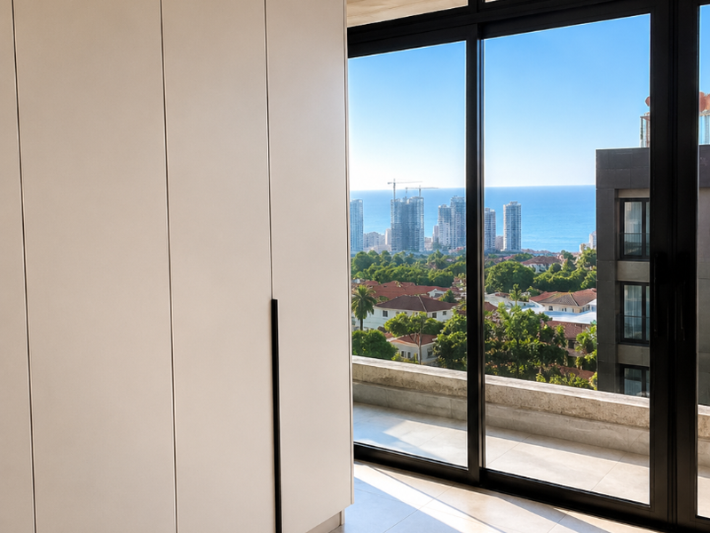 Modern bedroom featuring sleek built-in floor-to-ceiling wardrobes, large sliding glass doors, and expansive views of the city and ocean.