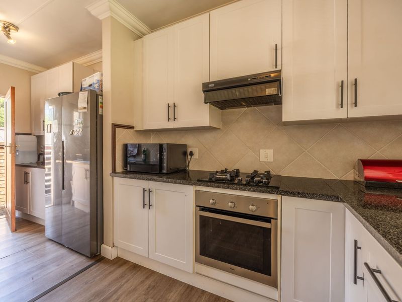 A well-maintained kitchen featuring white cabinetry, granite countertops, a gas hob, built-in oven, and a tiled backsplash, with direct access to the exterior.
