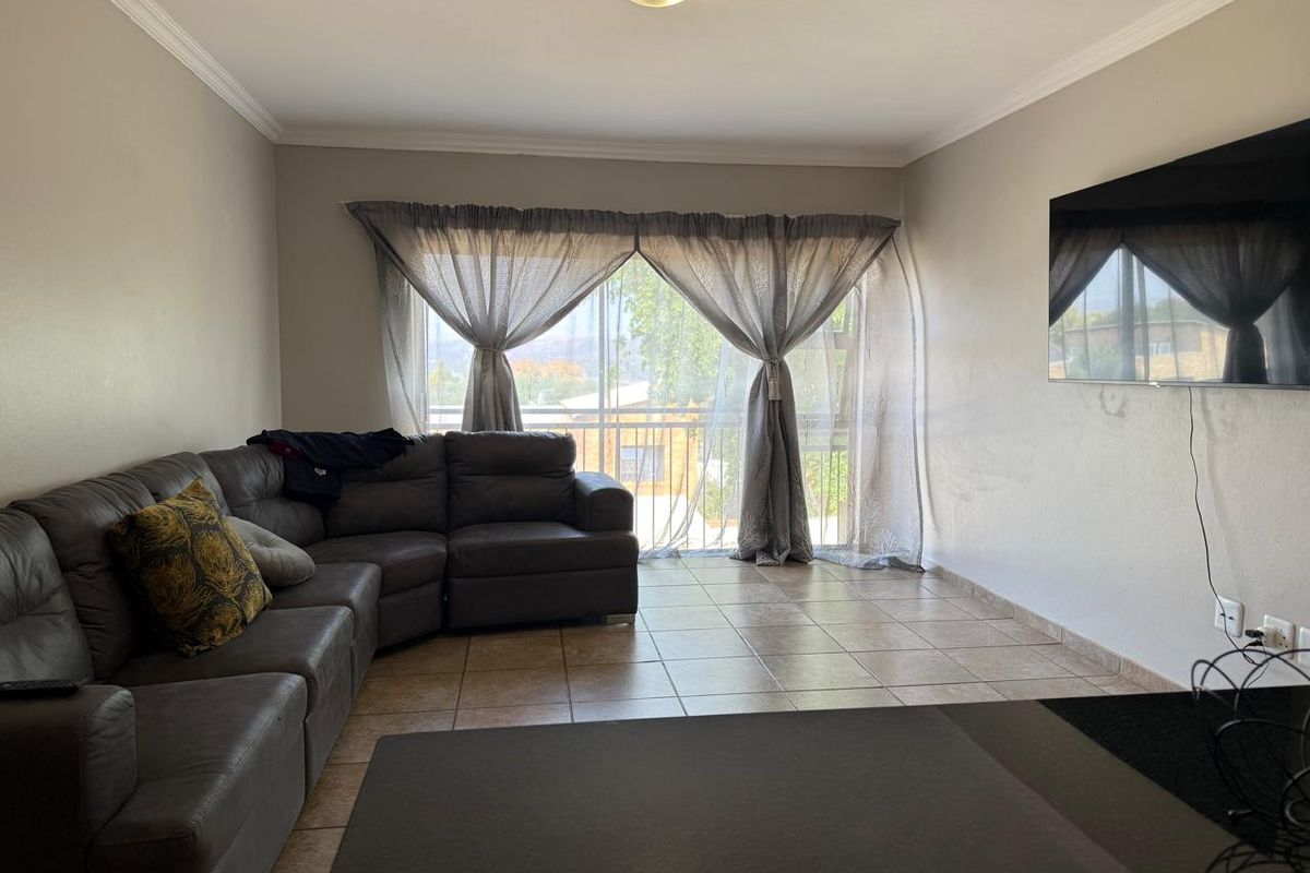 A living room featuring tiled flooring, crown molding, and a sliding glass door leading to a balcony, providing natural light and outdoor access.