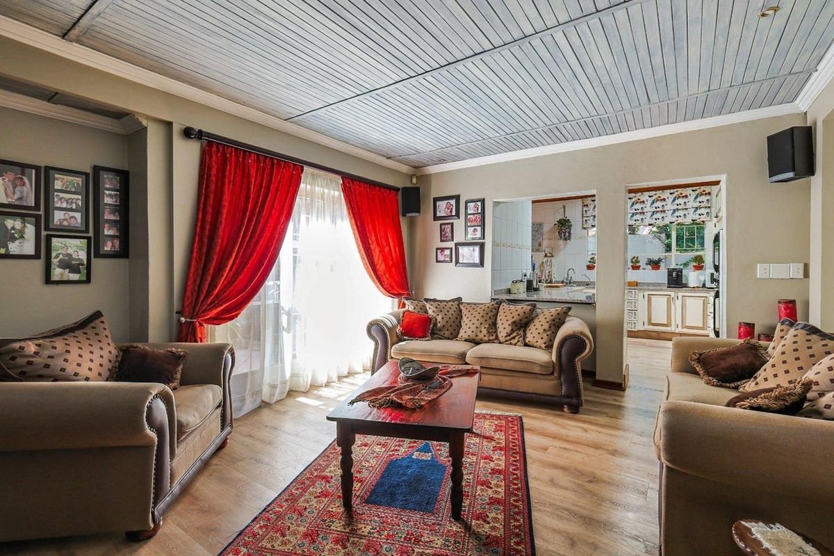 A comfortable living room featuring wood-look flooring and a unique paneled ceiling, with an open-plan flow leading into the adjacent kitchen area.