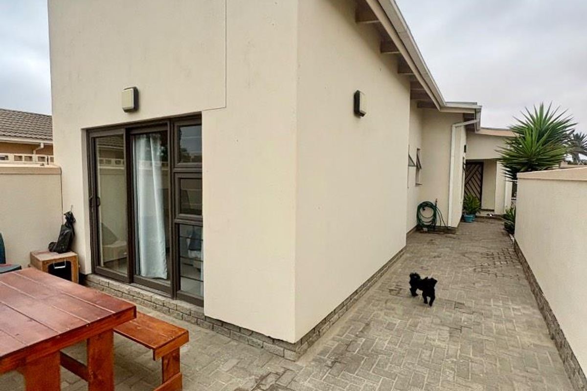 A rear exterior view of the townhouse featuring a paved courtyard area, sliding glass doors, and perimeter boundary walls.