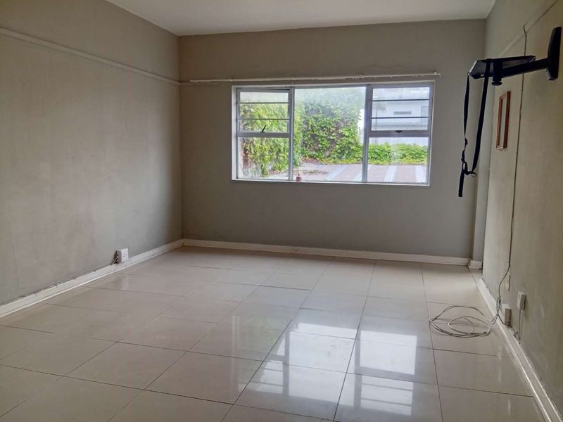 An empty living room featuring tiled flooring and large windows, providing a blank canvas for interior design and renovation.