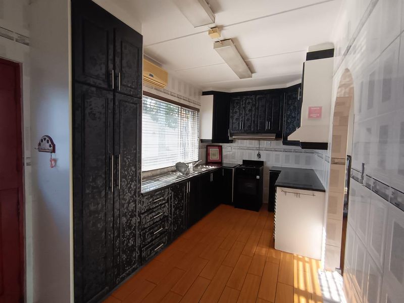 A functional kitchen featuring dark patterned cabinetry, a built-in stove with extractor fan, double sink, and tiled flooring.
