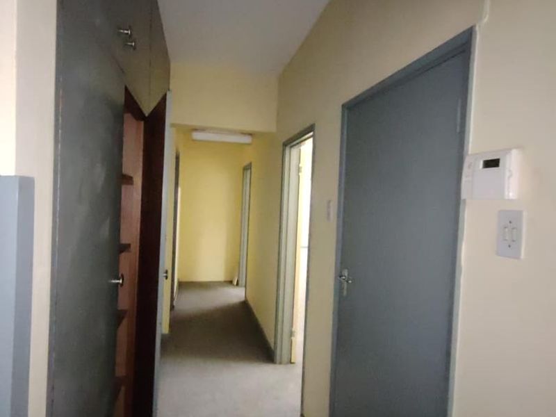 A functional hallway featuring built-in storage cupboards, multiple internal access doors, and a wall-mounted security alarm keypad.