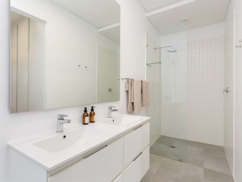 Modern bathroom featuring a double vanity with chrome fixtures, a large wall-mounted mirror, and a spacious walk-in shower with glass screen.