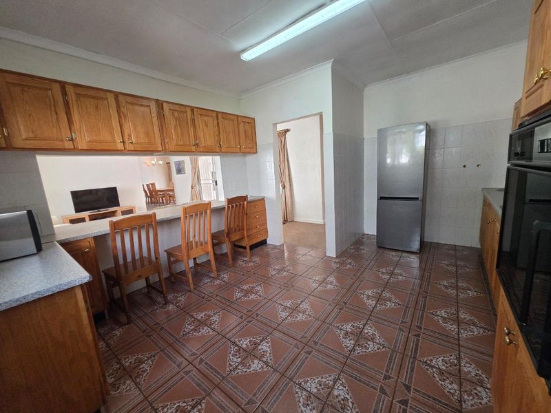 A functional kitchen featuring wooden cabinetry, tiled flooring, a breakfast bar, and built-in oven, offering a practical layout with direct access to adjacent living areas.