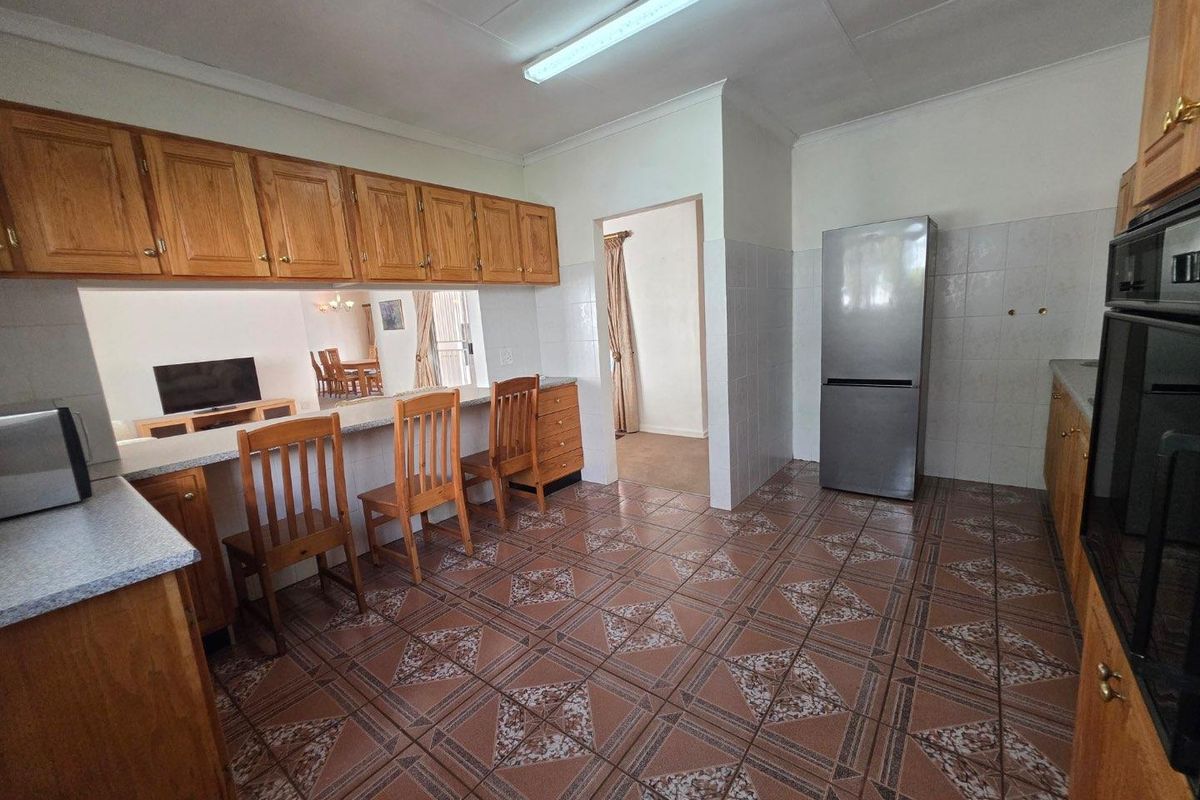 A functional kitchen featuring wooden cabinetry, tiled flooring, a breakfast bar, and built-in oven, offering a practical layout with direct access to adjacent living areas.
