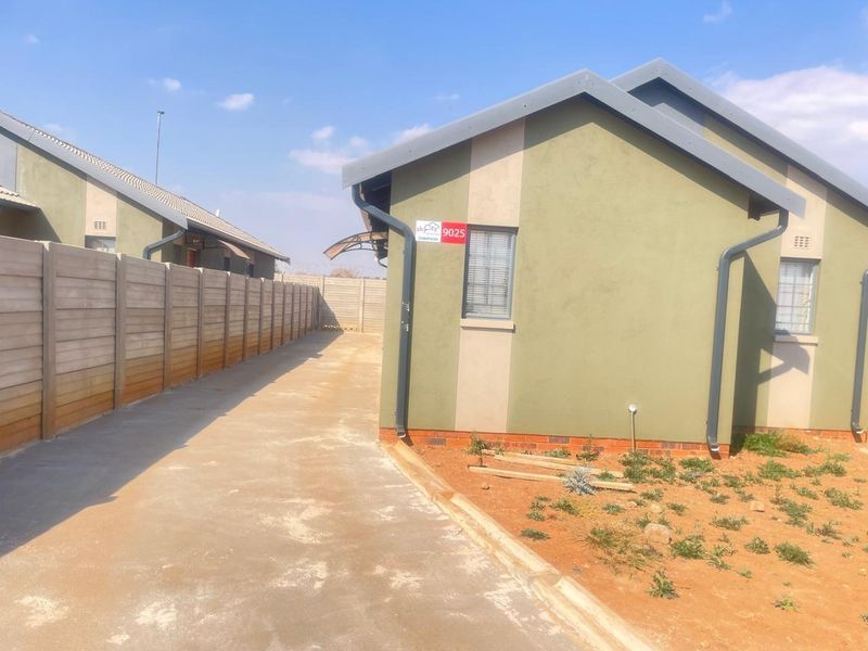 Side view of a residential property featuring a concrete driveway, precast boundary wall, and exterior wall finishes with aluminium window frames.