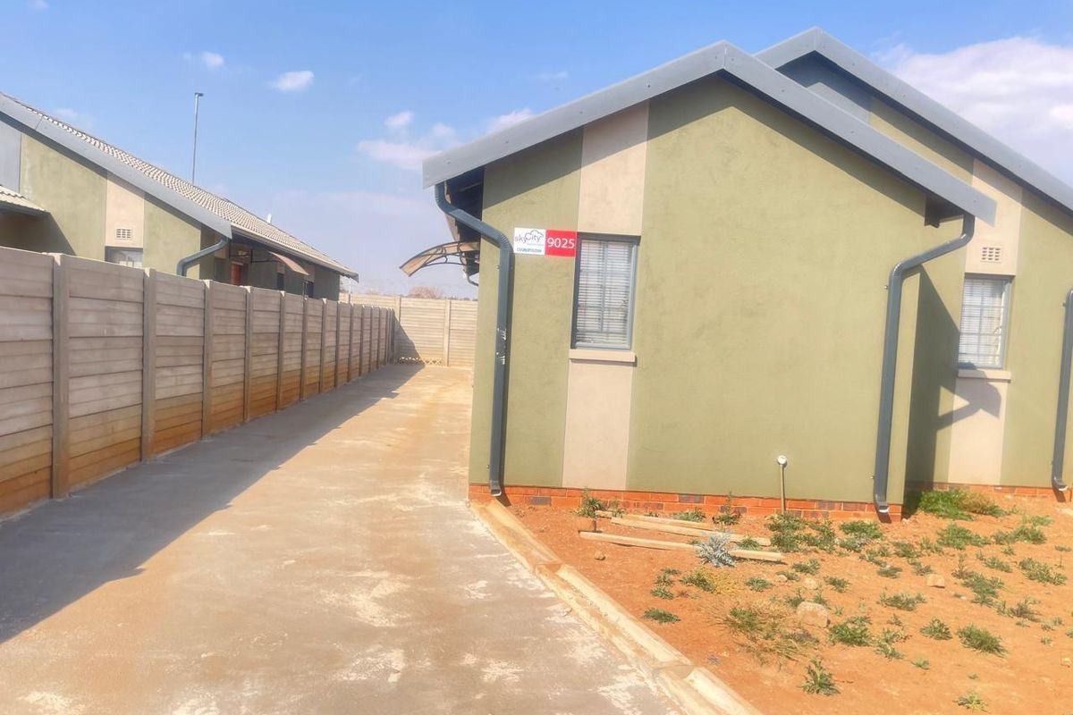 Side view of a residential property featuring a concrete driveway, precast boundary wall, and exterior wall finishes with aluminium window frames.