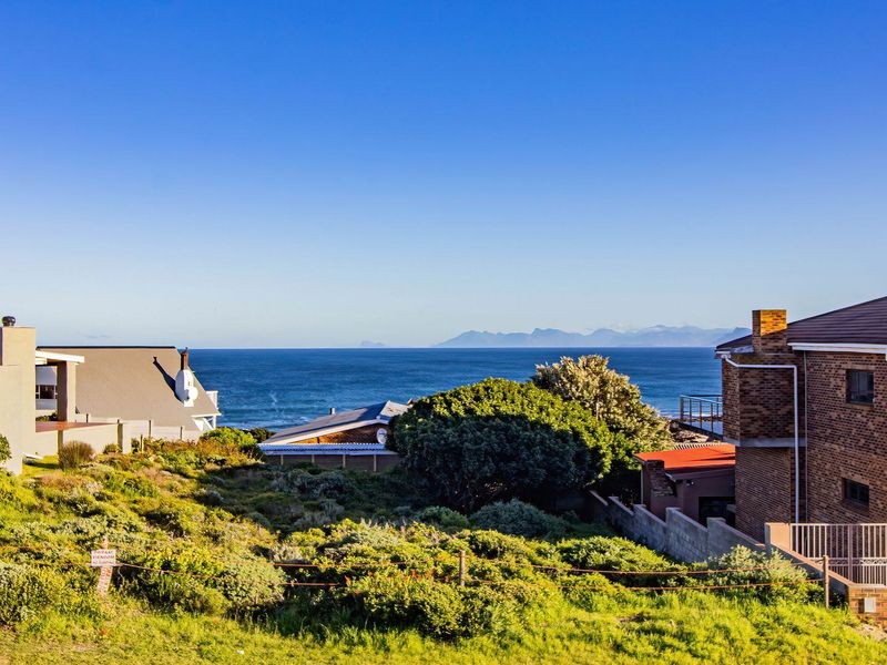 A scenic coastal view overlooking the ocean and distant mountains, featuring surrounding residential properties and landscaped garden areas.