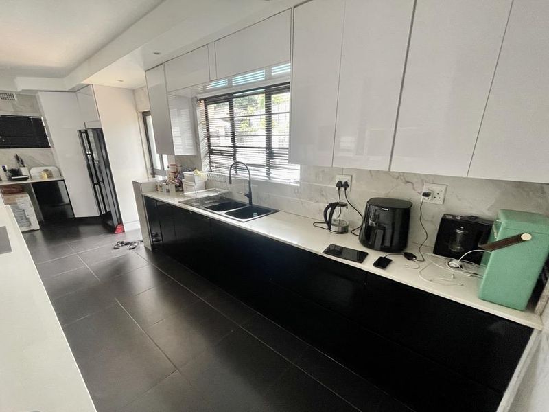 Modern kitchen featuring high-gloss white upper cabinets, contrasting black lower cabinetry, stone countertops, and a marble-look splashback with integrated sink.