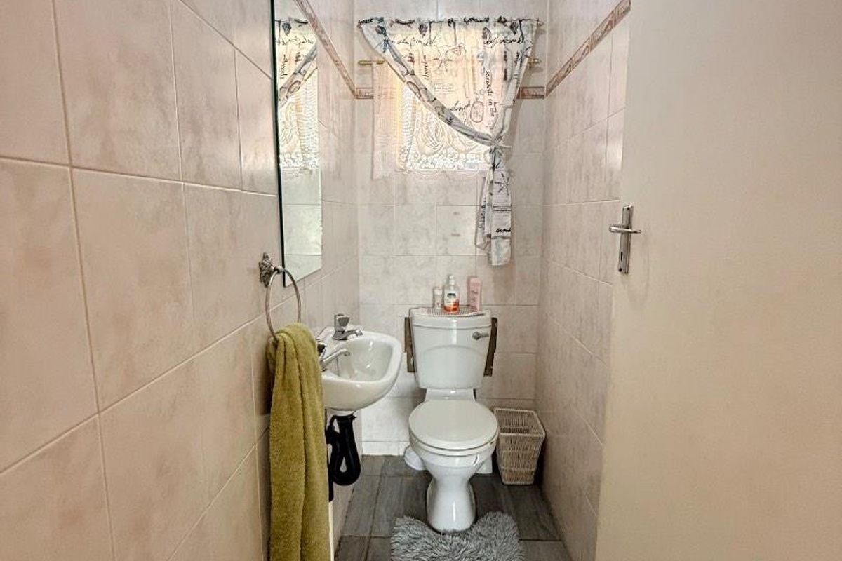 A compact guest bathroom featuring floor-to-ceiling wall tiles, a pedestal basin, and a standard toilet.