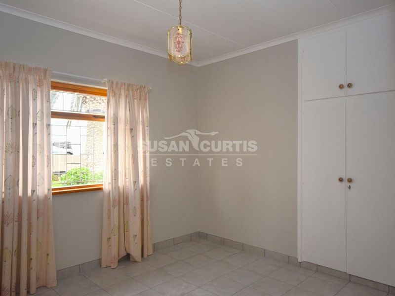 A clean, empty bedroom featuring neutral tiled flooring, built-in cupboards, and a window with security bars, offering a blank canvas for personalization.