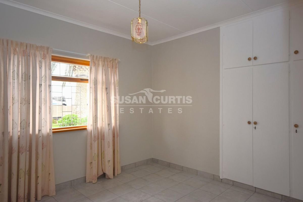 A clean, empty bedroom featuring neutral tiled flooring, built-in cupboards, and a window with security bars, offering a blank canvas for personalization.