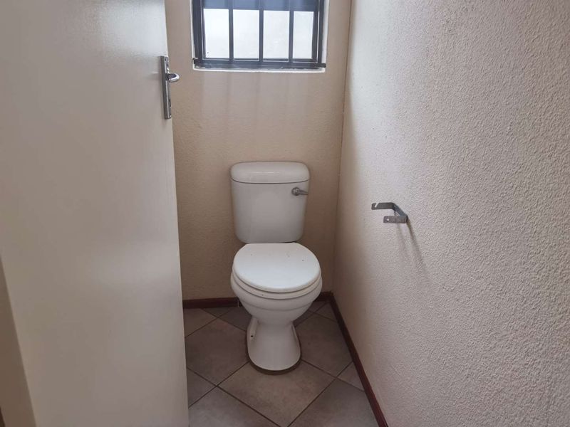 A small, functional guest toilet featuring tiled flooring and a security-barred window.