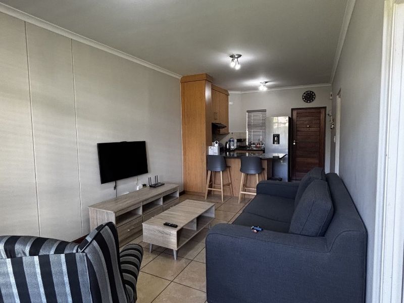 Open-plan living area featuring tiled flooring, a compact kitchen with breakfast bar, and neutral wall finishes, creating a functional and connected living space.
