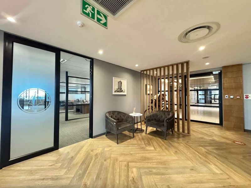 Modern office reception area featuring herringbone wood flooring, a decorative wooden slat divider, and professional glass-partitioned office spaces with integrated climate control.